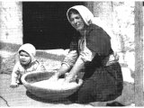 The dough which this Palestinian is kneading will be made into loaves baked upon the hot coals, and is not the thin biscuit-bread quickly cooked on the heated outside of the earthenware oven. An early photograph.